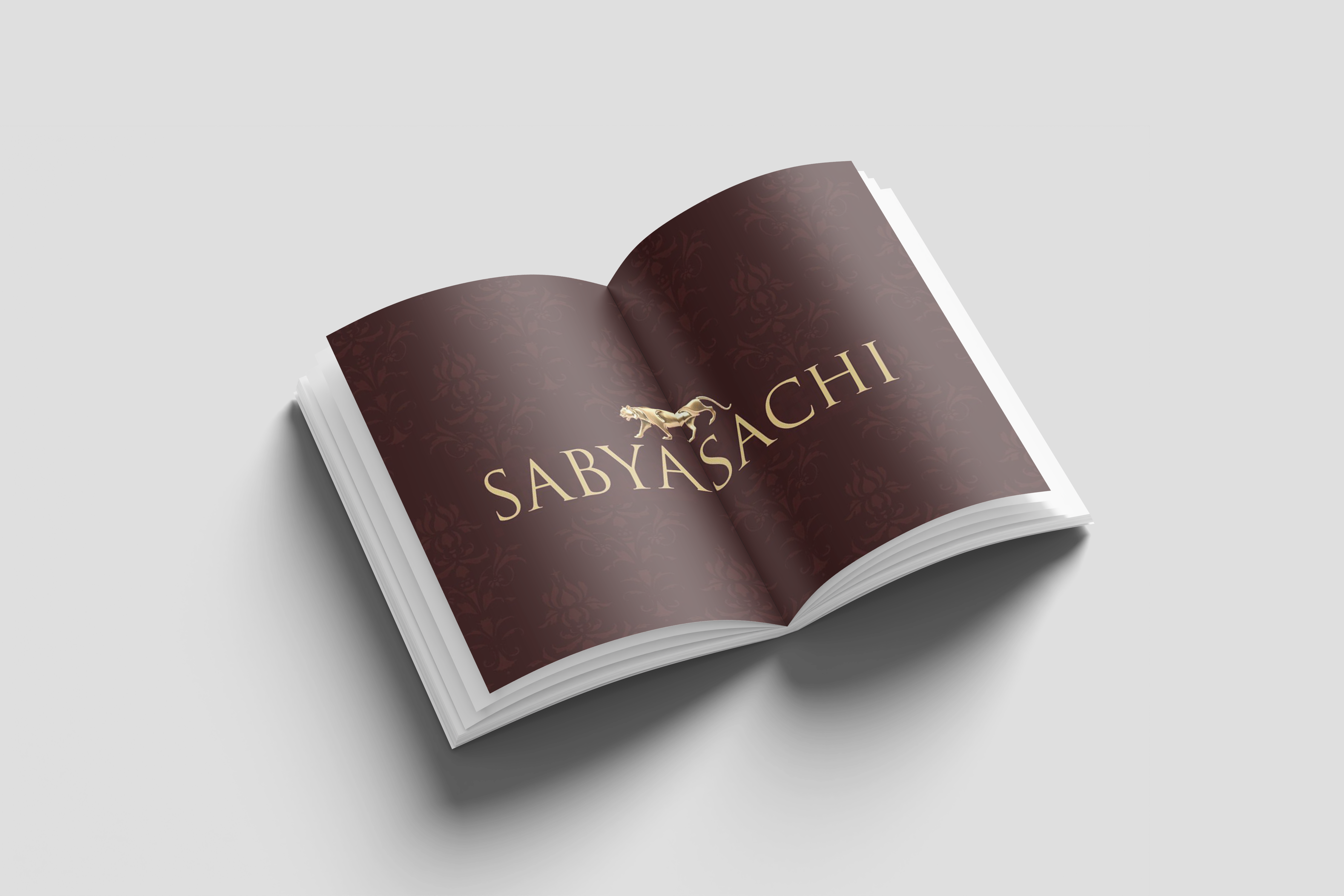 Open book with a maroon patterned spread and the gold Sabyasachi wordmark with a tiger